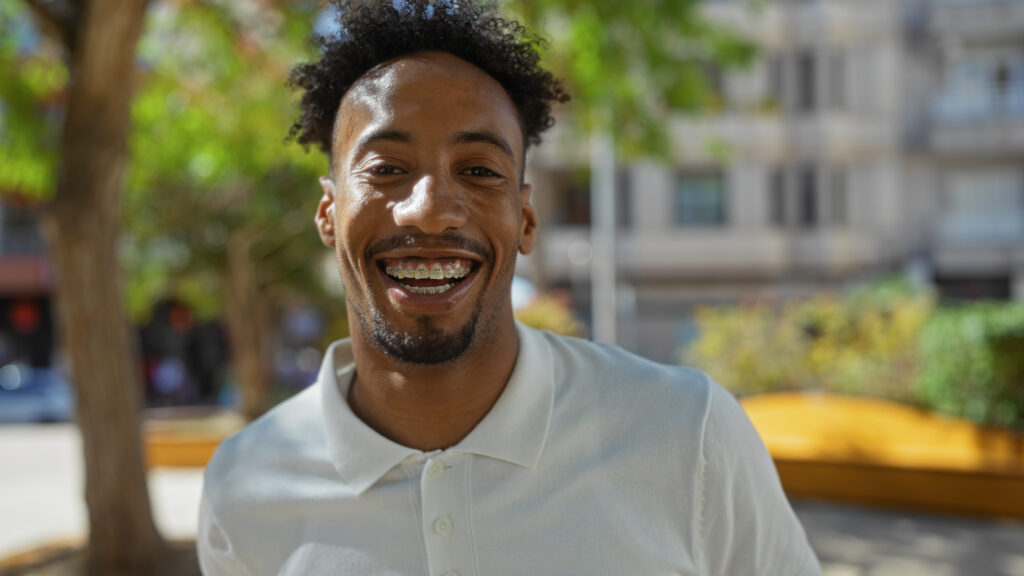 Handsome young african american man who has braces smiling in an urban park setting on a sunny day.