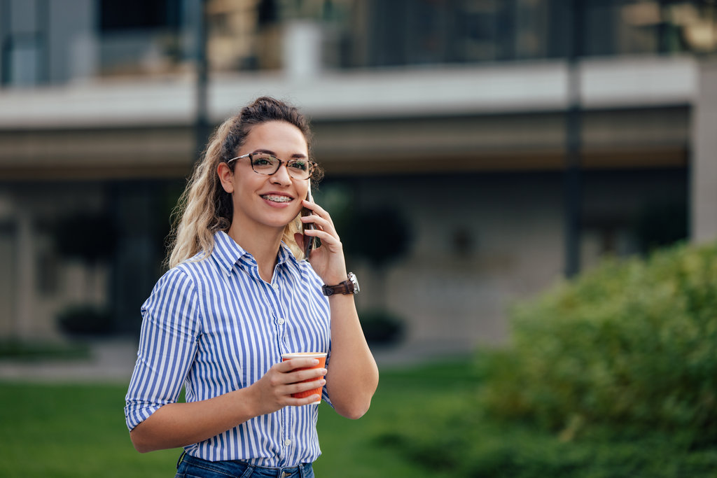 Blonde girl making a phone call, walking on the street, holding a cup of coffee.