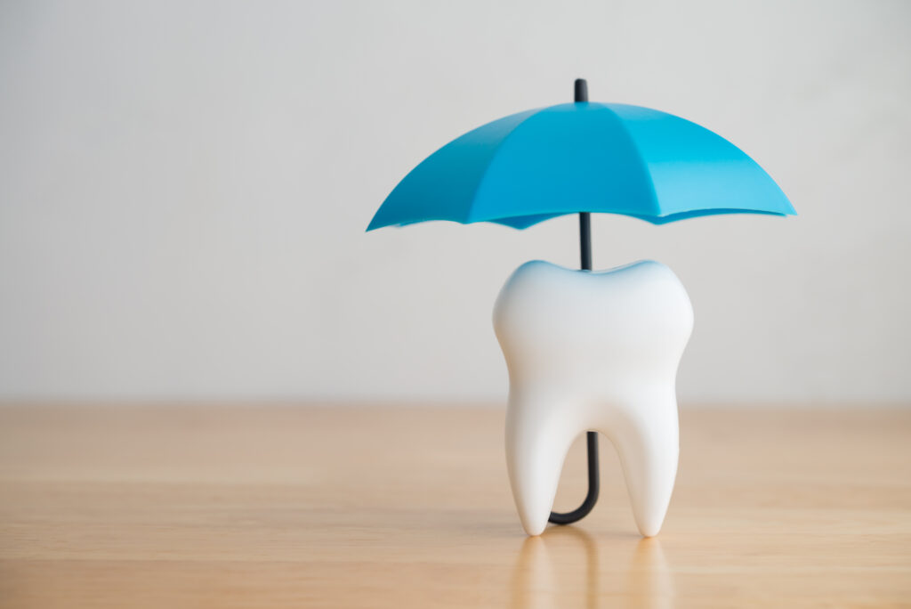 Blue umbrella covers white clean tooth on white background. Dental insurance, dental care, tooth protection concept. Dental health insurance is a contract that helps pay for dental care costs.