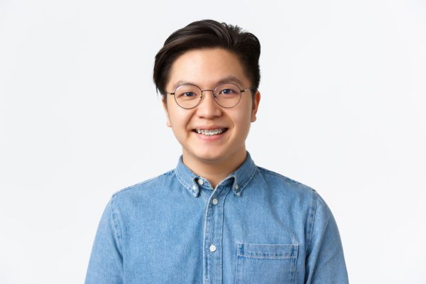 Close-up of hopeful cute asian guy with braces smiling at camera, satisfied with professional dental care at stomatology clinic, looking pleased, standing over white background.