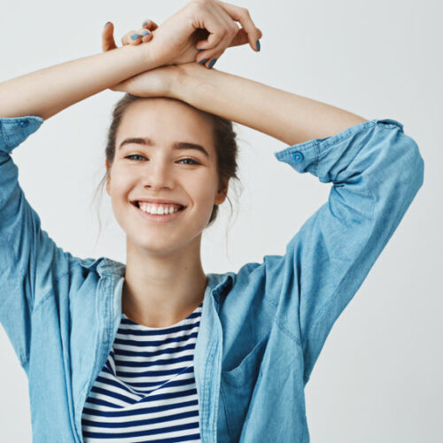 Do not worry be happy. Portrait of gorgeous girlfriend in love, holding crossed arms on forehead, standing in sensual pose, smiling broadly at camera and expressing positive and tender emotions. Copy space