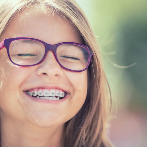 Portrait of a happy smiling teenage girl with dental braces and glasses.