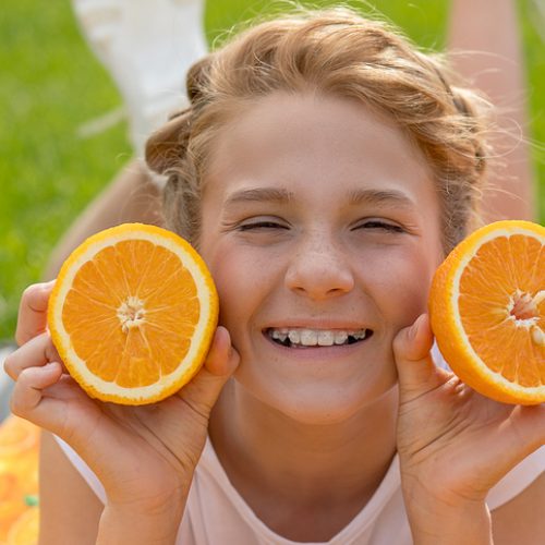 Beautiful teenage girl with two oranges in hands. She smiles broadly and laughs with ceramic braces on teeth. She is not shy about them. Concept of dentistry, dental orthopedics. Healthy diet photo Beautiful teenage girl with two oranges in her hands. She smiles broadly and laughs with ceramic braces on teeth. Not shy about them. Concept of dentistry, dental orthopedics. Healthy diet photo