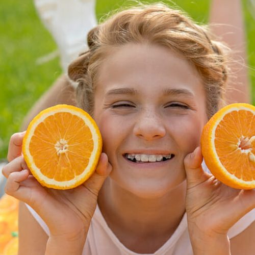 Beautiful teenage girl with two oranges in her hands. She smiles broadly and laughs with ceramic braces on teeth. Not shy about them. Concept of dentistry, dental orthopedics. Healthy diet photo