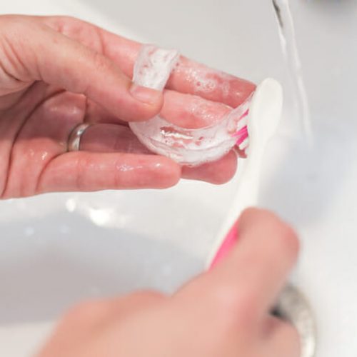 woman's hands washing her invisible aligners for dental correction with soap and water