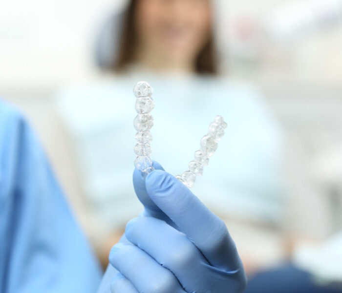 Dentist hand with gloves holding a silicone trainer in a consultation with a patient in the background